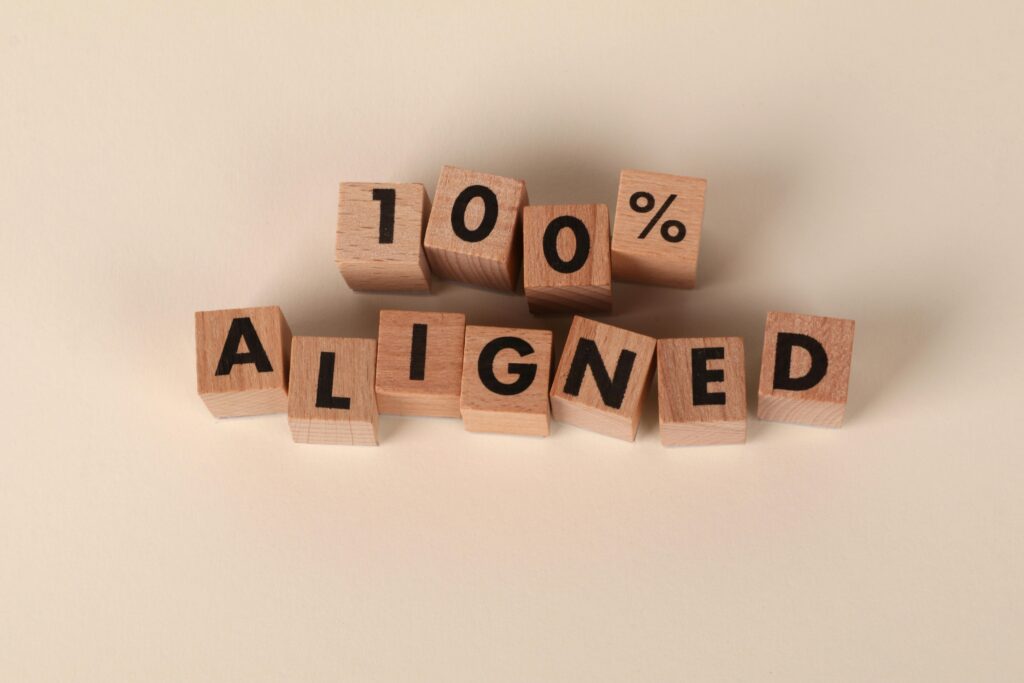 Alignment Is the Hidden Key to Sustainable Success Wooden blocks spelling '100% Aligned' on a neutral background, conveying precision and alignment.