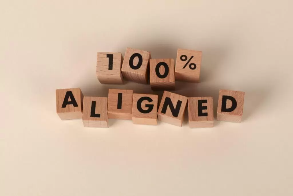 Alignment Is the Hidden Key to Sustainable Success Wooden blocks spelling '100% Aligned' on a neutral background, conveying precision and alignment.